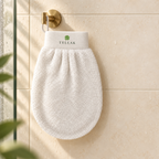 Tellak hammam exfoliating mitt hanging from a brass hook on a cream tiled shower wall