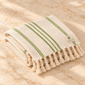 Folded cream Tellak peshtemal towel with olive green stripes and twisted tassels