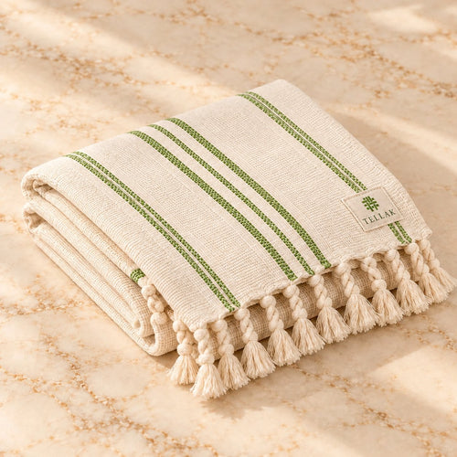 Folded cream Tellak peshtemal towel with olive green stripes and twisted tassels